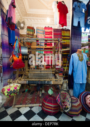 Uomo che utilizza un telaio di tessitura in un negozio di abbigliamento a Tangeri, Marocco Foto Stock