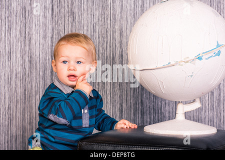 Adorabili curioso baby boy studiando il modello di un mondo indoor Foto Stock