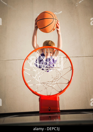 Ragazzo caucasico dunking basket in hoop Foto Stock