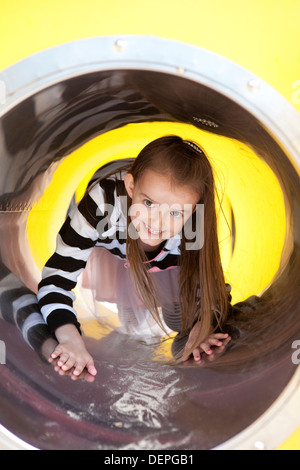 Ragazza giovane giocare felicemente e strisciando attraverso un tunnel di giocare in un parco giochi. Foto Stock