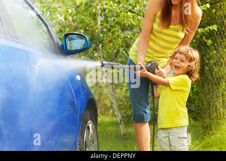 Madre e tre anni figlio auto lavaggio con idropulitrice ad alta pressione con ragazzo puntando ugello di acqua in piedi fuori nel parcheggio yeard Foto Stock