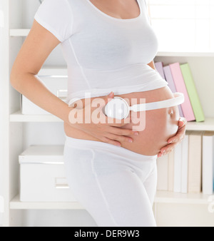 Donna incinta mettendo le cuffie sul suo ventre. Gravidanza relax a casa. Foto Stock