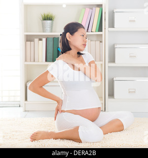 Spalla o dolore al collo. Otto mesi di gravidanza donna asiatica tenendo la schiena e la spalla mentre è seduto su un pavimento a casa. Foto Stock