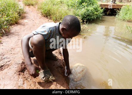 Un giovane ragazzo raccoglie acqua sporca da un fiume nel distretto di Luwero dell Uganda. Foto Stock