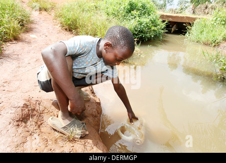 Un giovane ragazzo raccoglie acqua sporca da un fiume nel distretto di Luwero dell Uganda. Foto Stock