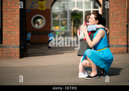 Un attraente felice giovane mamma consolante e di prelevare o far cadere la figlia presso la scuola infantile gates Foto Stock