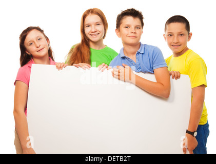 Il gruppo di quattro sorridenti amici, due ragazze e due ragazzi, tenendo vuoto bianco pubblicità segno vicino ritratto Foto Stock