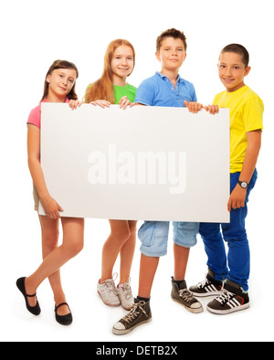 Quattro sorridenti amici, due ragazze e due ragazzi, tenendo vuoto bianco pubblicità segno in piedi di altezza piena Foto Stock