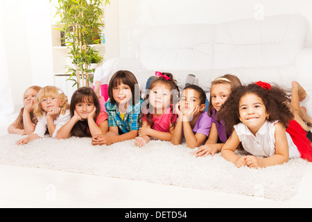 Gruppo di otto bambini, ragazzi e ragazze, nero, asiatici e caucasici la posa sul pavimento in casa nel salotto guardando la fotocamera Foto Stock