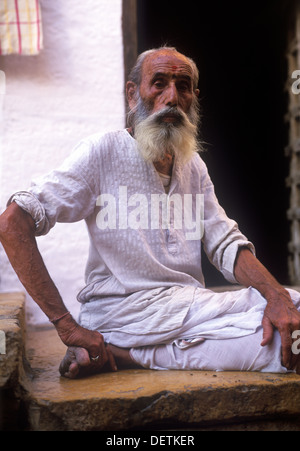 Long-barbuto anziano uomo vestito di dhoti, seduti nella parte anteriore della porta. Jaiselmer, Rajasthan, India Foto Stock