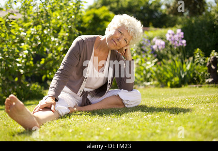 Donna matura di sedersi sull'erba comodamente in giardino guardando a voi - all'aperto Foto Stock