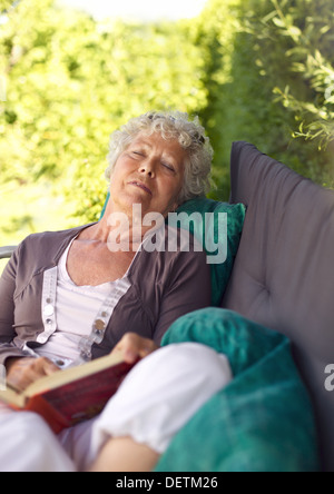 Senor donna seduta sulla poltrona con un libro e parlare di un NAP. Senior lady dormire nel cortile interno con un romanzo Foto Stock