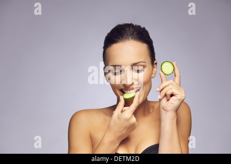 Ritratto di un attraente giovane donna di mangiare una fetta di cetriolo. Sano giovane signora sorridente con fette di cetriolo Foto Stock