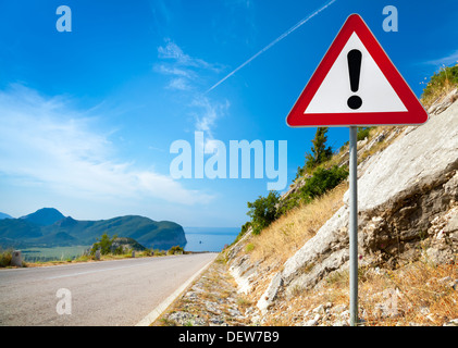 Avvertenza cartello stradale con un punto esclamativo in un triangolo rosso sulla autostrada di montagna Foto Stock