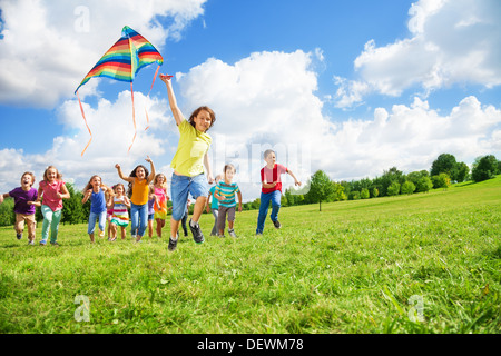 Ragazzo in esecuzione con kite con un grande gruppo di amici, di ragazzi e ragazze in esecuzione dopo Foto Stock