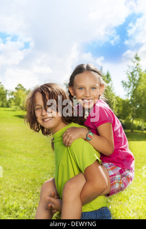 Ragazzo portano la ragazza sulla sua schiena, sia felice e sorridente, nel parco sulla soleggiata giornata estiva Foto Stock