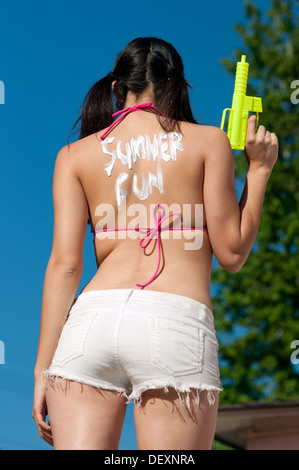 La donna vista posteriore con sun lozione blocco scrittura azienda pistola ad acqua estate in un momento di divertimento Foto Stock
