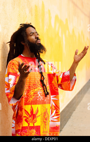 Dreadlocks uomo nero sollevare palme fino a lode di Dio ritratto colorato Foto Stock