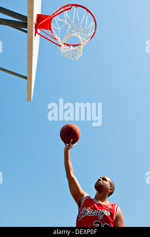 African American giocatore di basket tenere la pallacanestro mirando a outdoor Basketball hoop Foto Stock