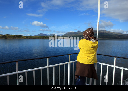 Donna con giallo giacca impermeabile e brown spotted velo su un traghetto Calmac avvicinando il Castello di Duart sull'Isle of Mull Foto Stock