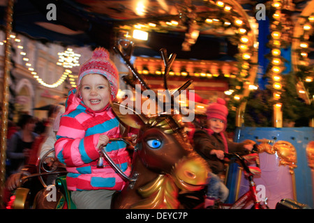 Bambina di tre anni, a cavallo di una giostra ad un mercatino di Natale Foto Stock