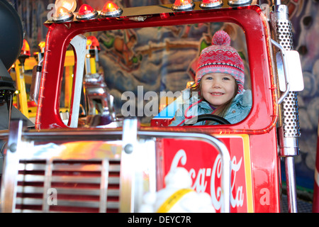 Bambina di tre anni, in sella a un carrello su una giostra a un mercato di Natale Foto Stock