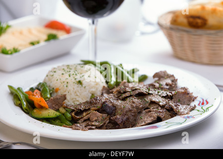 Gyro Döner guarnita con riso Pilaf verdure e collaborato con hummus, pane pita e vino rosso Foto Stock