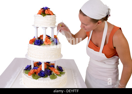 Baker signora con un bianco bandana dando ad una torta di nozze i tocchi finali, torta ha fondente volant sul lato e decorate Foto Stock