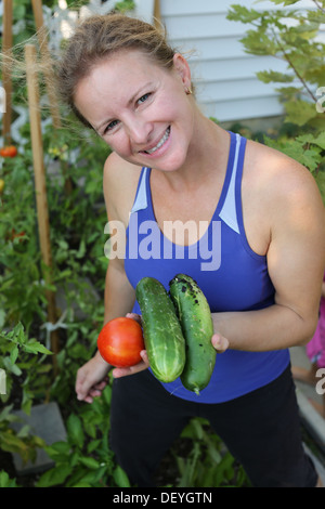 Donne di mezza età la raccolta di sua organica coltivati pomodori e cetrioli dal suo giardino verde. Foto Stock