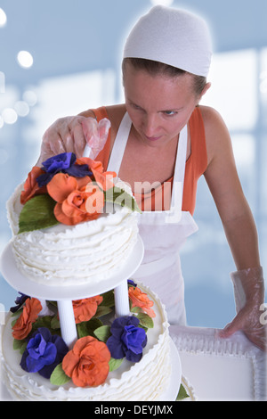 Donna con il bianco bandana dando ad una torta di nozze ultimi ritocchi di piccole dimensioni Foto Stock