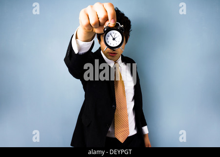 Giovane uomo d affari tenendo una sveglia davanti al suo volto Foto Stock