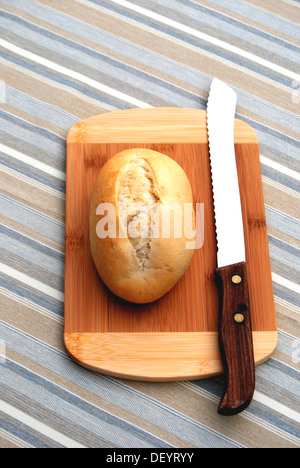 Rotolo di pane su una tavola di legno, tagliere, coltello per pane, striato tovaglia Foto Stock