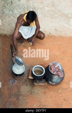 Rurale villaggio indiano uomo la cottura del riso su un bastone aperto il fuoco dal di sopra. Andhra Pradesh, India Foto Stock