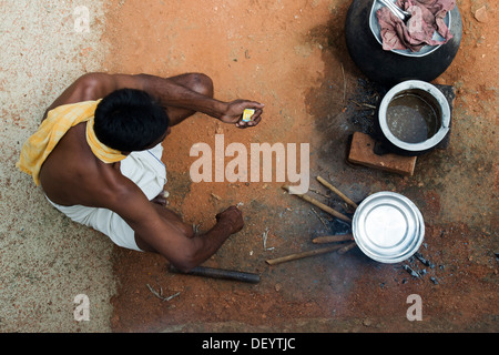 Rurale villaggio indiano uomo la cottura del riso su un bastone aperto il fuoco dal di sopra. Andhra Pradesh, India Foto Stock