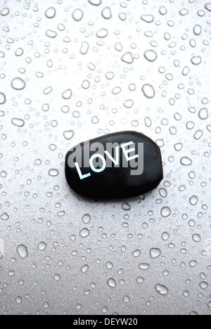 Massaggio hot stone pietra con la scritta amore su una superficie con gocce d'acqua Foto Stock