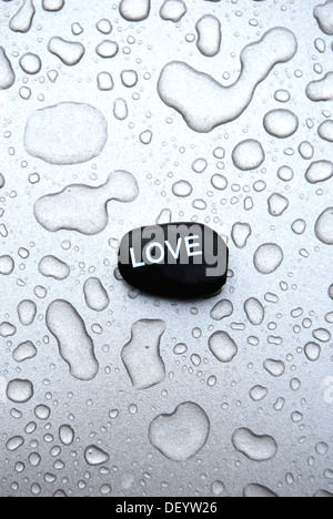Massaggio hot stone pietra con la scritta amore su una superficie con gocce d'acqua Foto Stock
