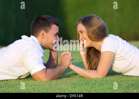 Profilo di un giovane in amore flirt e cerca ogni altra sdraiati sull'erba con uno sfondo verde Foto Stock