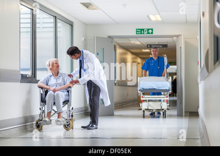 Infermiere spingendo barella barella letto nel corridoio di ospedale con medico & senior paziente femmina Foto Stock