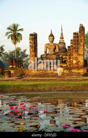 Seduto statua del Buddha dietro un laghetto con Red Water Lilies (Nymphaea rubra), Wat Mahathat tempio, Sukhothai Historical Park Foto Stock