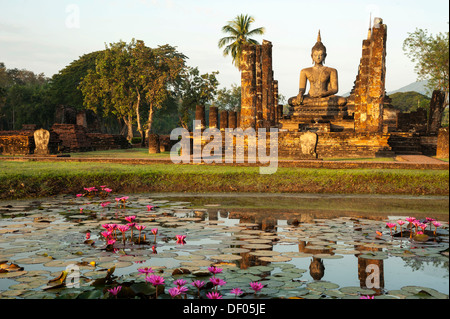 Seduto statua del Buddha dietro un laghetto con Red Water Lilies (Nymphaea rubra), Wat Mahathat tempio, Sukhothai Historical Park Foto Stock