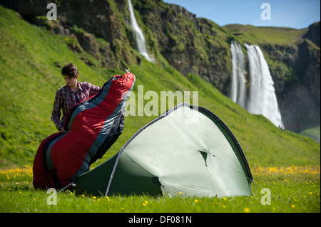 Donna con un sacco a pelo e una tenda, Seljalandsfoss cascata presso il fiume Seljalandsá, Ring Road, Suðurland, Sud Islanda Foto Stock