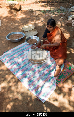 Rurale villaggio indiano donna utilizzando pietre Quern per macinare il miglio di dito seme / Ragi semi in Ragi farina. Andhra Pradesh. India Foto Stock