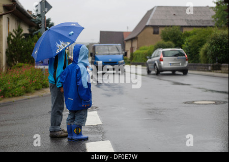 Due bambini di 4 e 8 anni, in attesa di attraversare la strada sotto la pioggia, due automobili, Assamstadt, Baden-Wuerttemberg Foto Stock