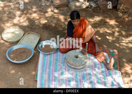 Rurale villaggio indiano donna utilizzando pietre Quern per macinare il miglio di dito seme / Ragi semi in Ragi farina. Andhra Pradesh. India Foto Stock