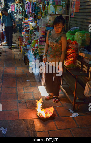 Negoziante bruciando buona fortuna preghiere per lei in stallo il mercato russo, Phnom Penh Cambogia Foto Stock