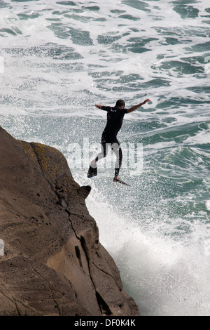 Un uomo salta fuori da una scogliera in mare. Foto Stock