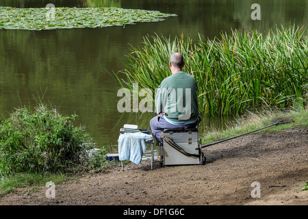 Un pescatore che pesca in Old Hall stagno a Thorndon Country Park in Essex. Foto Stock