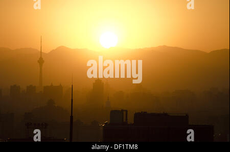 Il sole tramonta in un intenso bagliore arancione a causa dell'inquinamento atmosferico e della foschia, con una parte dello skyline visibile di fronte alle colline profumate, come si vede qui dal centro di Pechino durante la fine dell'estate. © Olli Geibel Foto Stock