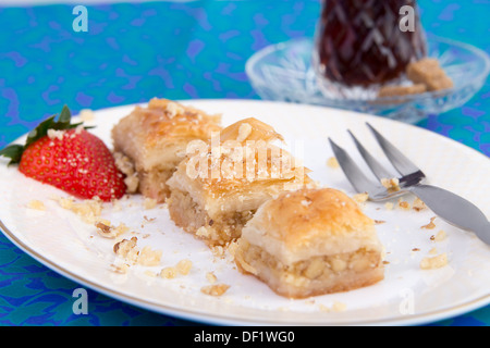 Tre pezzi di colore dorato baklava guarnita con noci e fragola e servito in forma ovale piastra sul verde e blu colo Foto Stock