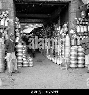 Foto storica,1950 da J Allan Cash, di un giovane maschio afghano in piedi da una bancarella di mercato coperto di strada o bazar in Kabul, Afghanistan, dove una grande varietà di barattoli di metallo, pentole e padelle sono in vendita. Foto Stock